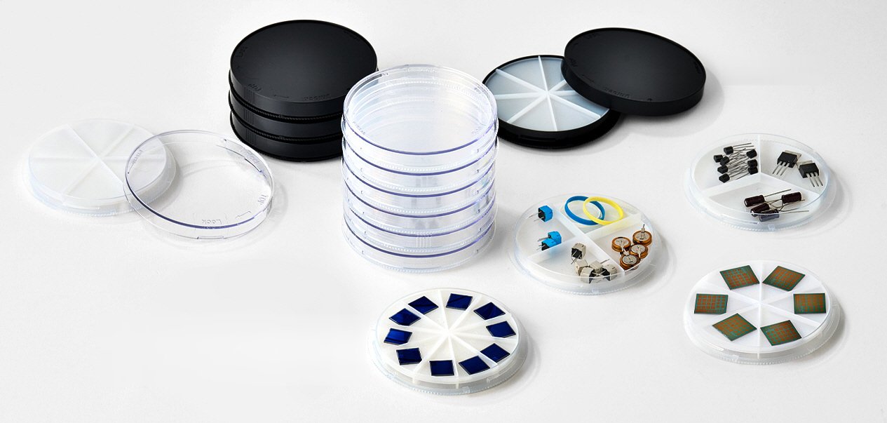 Transparent and black Petri dishes by PYBLab, stacked and open, some fitted with partitions holding electronic components, rubber rings and semiconductor chips